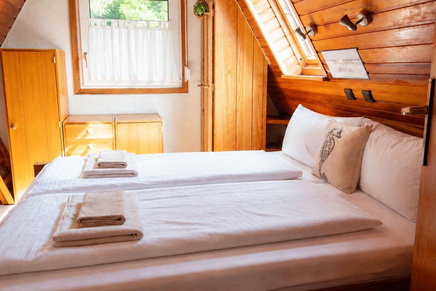 Schlafzimmer mit Doppelbett, Holzmöbeln, Dachfenster und schräger Holzdecke.
