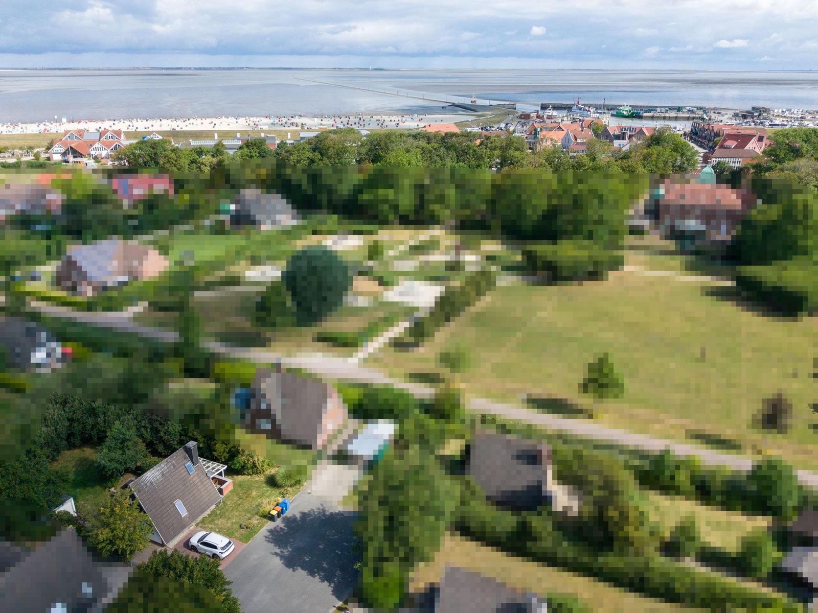Luftbild von Häusern mit Gärten, Sandstrand mit Strandkörben und Booten.