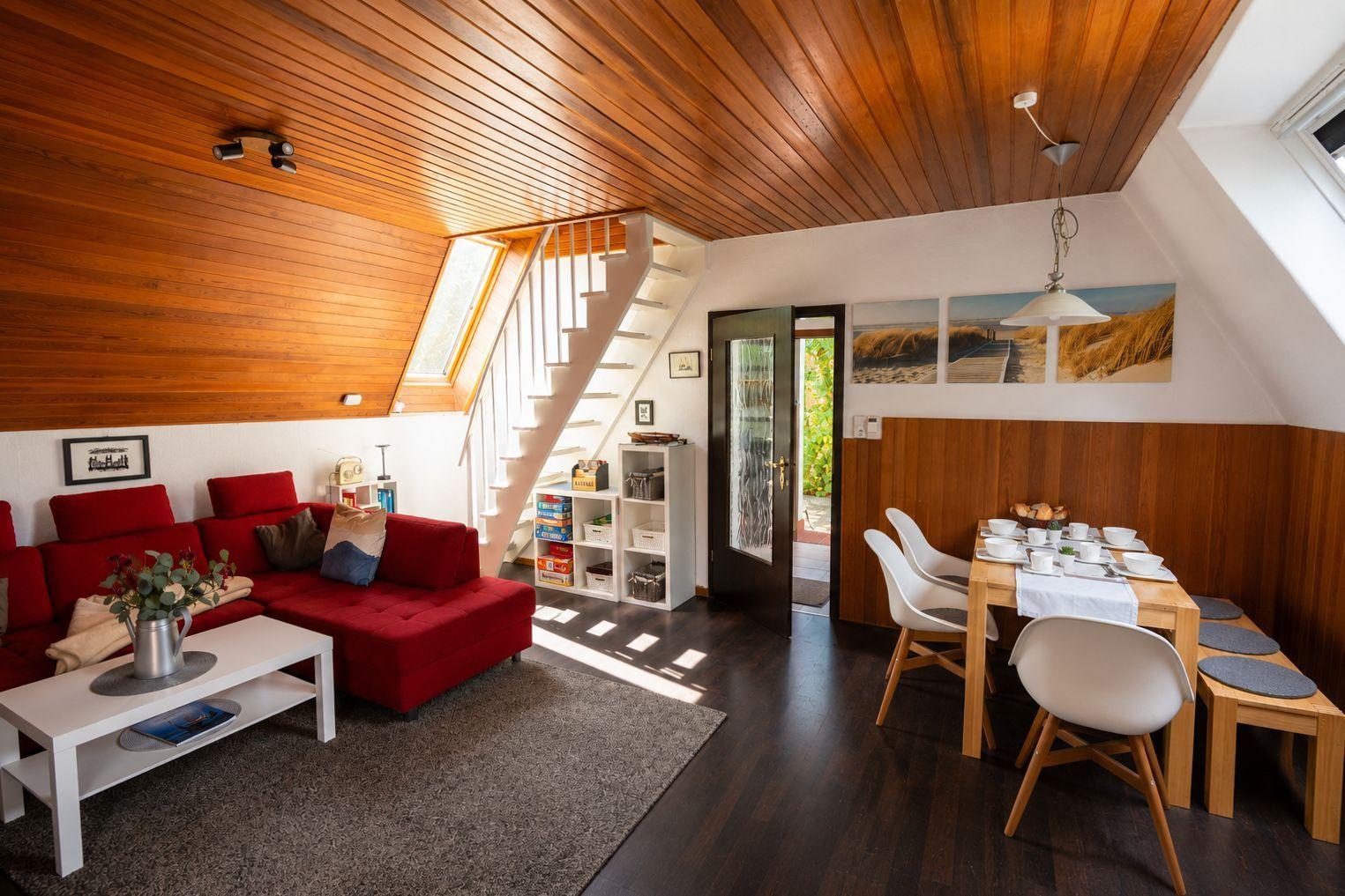 Wohn-Essbereich mit rotem Sofa, Holztisch, weißer Treppe und Holzdecke.