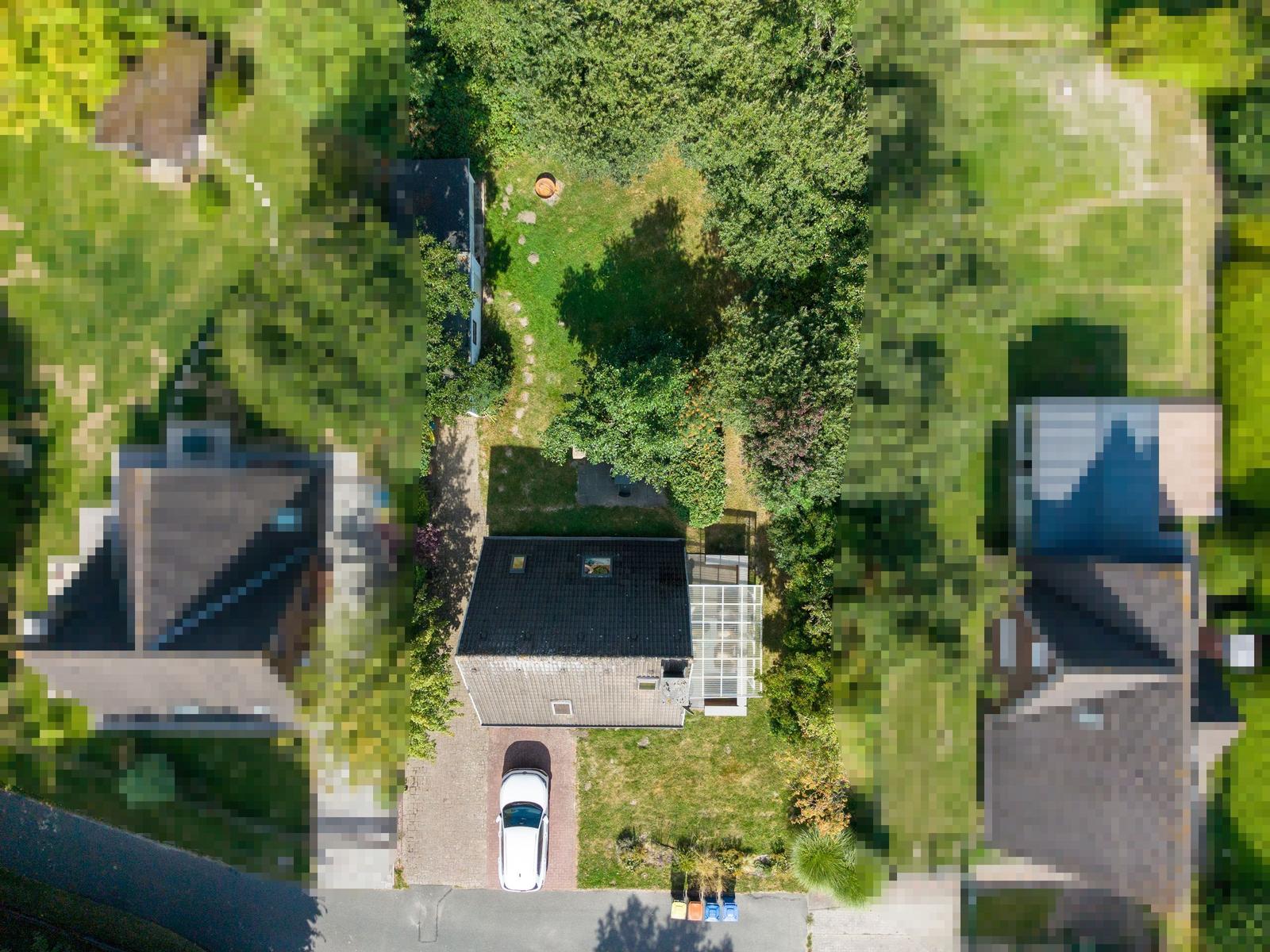Luftbild von oben auf Haus mit dunklem Dach, Garten, Terrasse und Auto.