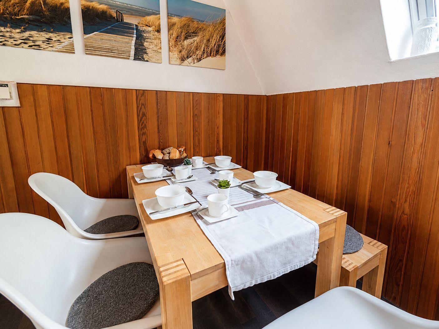Holztisch mit Gedeck, weißen Stühlen, Holzbank und drei Strandmotiven an der Wand.