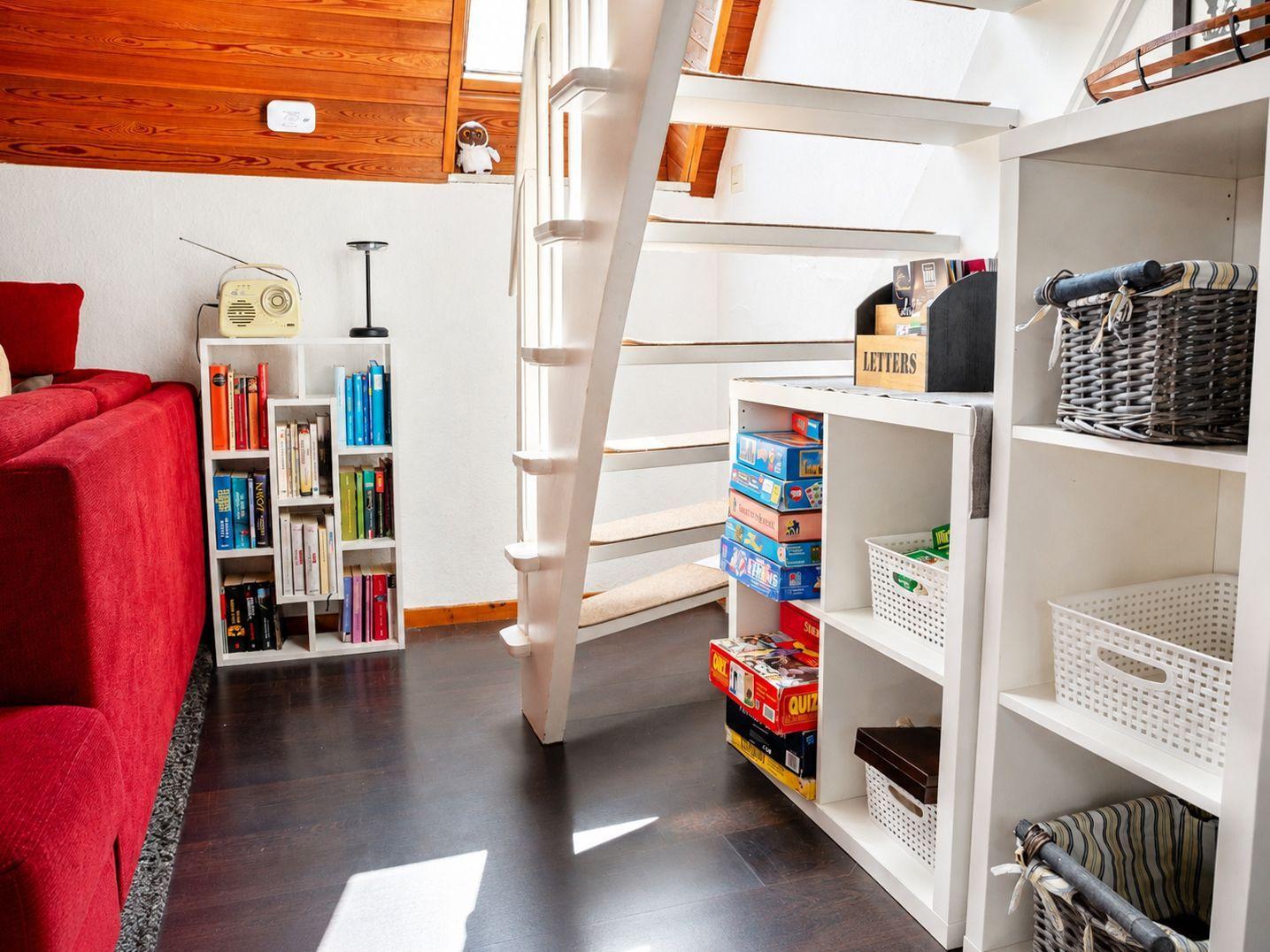 Weiße Treppe mit Regalen, Brettspielen und Körben neben einem roten Sofa.