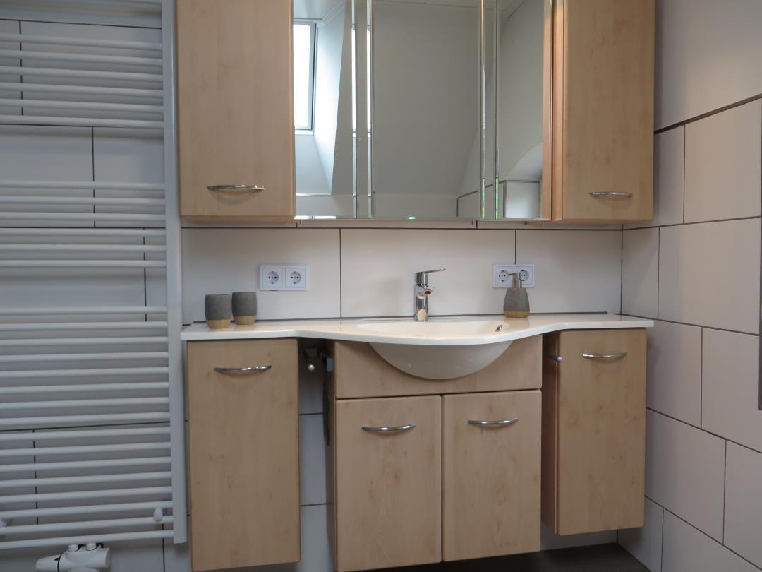Badezimmer mit Waschtisch aus hellem Holz, Spiegelkasten und Handtuchheizkörper.