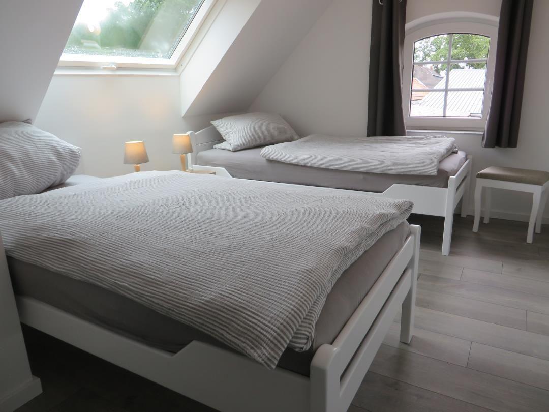 Dachzimmer mit zwei Einzelbetten, Dachfenster und rundem Bogenfenster.
