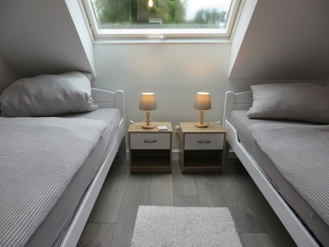 Dachzimmer mit zwei Einzelbetten, Nachttischen und großem Dachfenster.