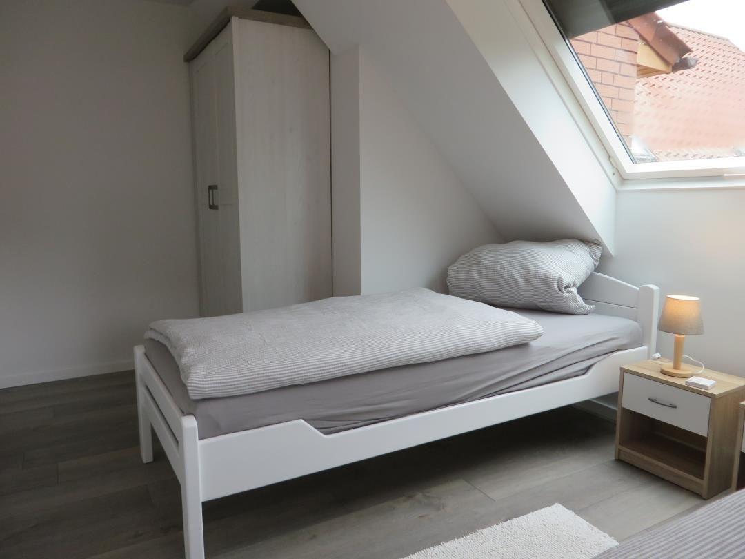 Dachzimmer mit Einzelbett, Nachttisch, Schrank und Dachfenster.