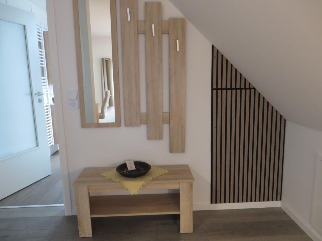 Flur unter Dachschräge mit Holzbank, Spiegel und Garderobe.