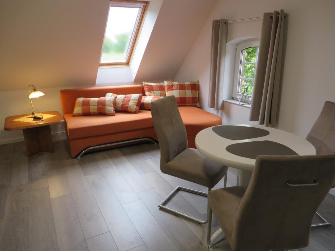 Dachwohnzimmer mit orangem Sofa, rundem Esstisch und Dachfenster.