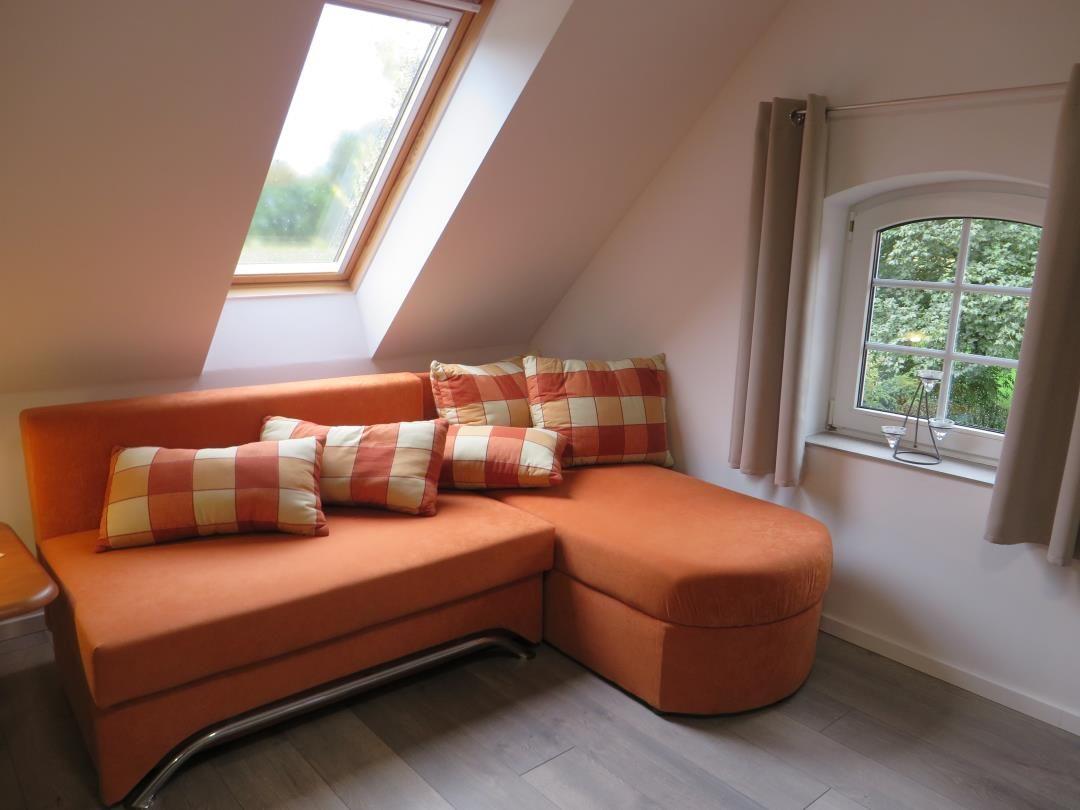 Orangefarbenes Ecksofa mit Karokissen unter Dachschräge und Dachfenster.