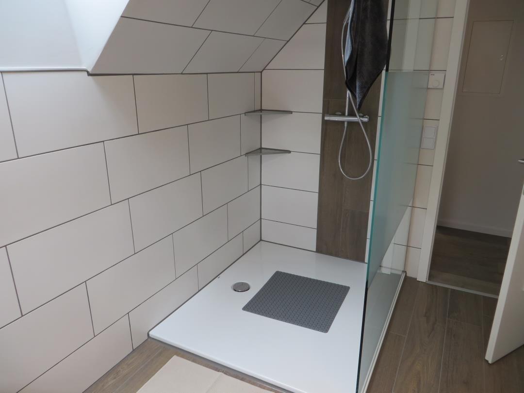 Begehbare Dusche mit weißen Fliesen, Holzoptik und Glaswand unter Schräge.