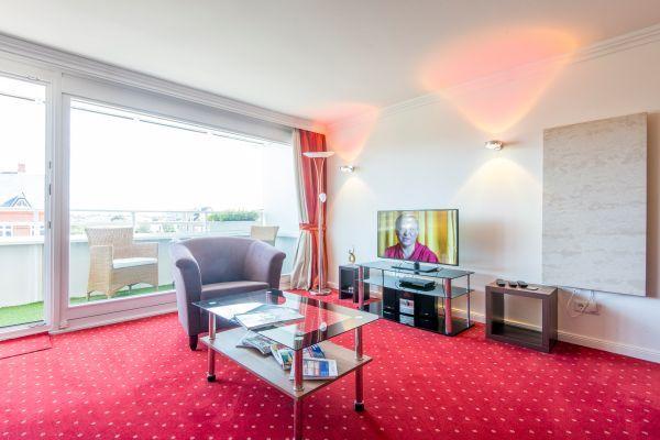 Wohnzimmer mit rotem Teppich, Glastisch, Sessel und Fernseher