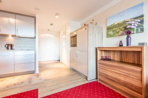 Blick zu Küche und Flur, Sideboard mit Vasen und Wandbild, roter Teppich.