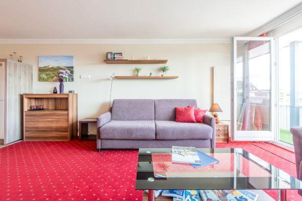 Wohnzimmer mit lila Sofa, roten Kissen, Wandregalen und rotem Teppich.