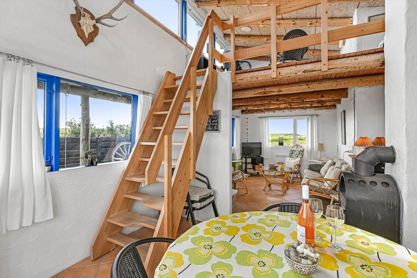 Essbereich mit rundem Tisch, Holztreppe zur Empore, Sofa und Kaminofen.