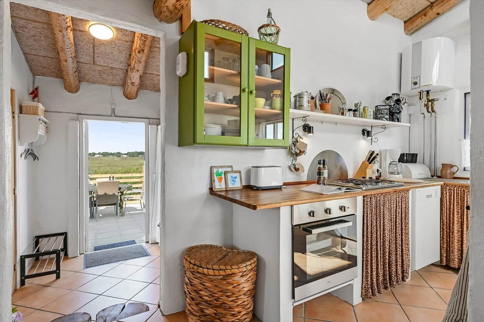 Küche mit Holzplatte, Backofen, Gasherd, grünem Schrank und Terrassentür.
