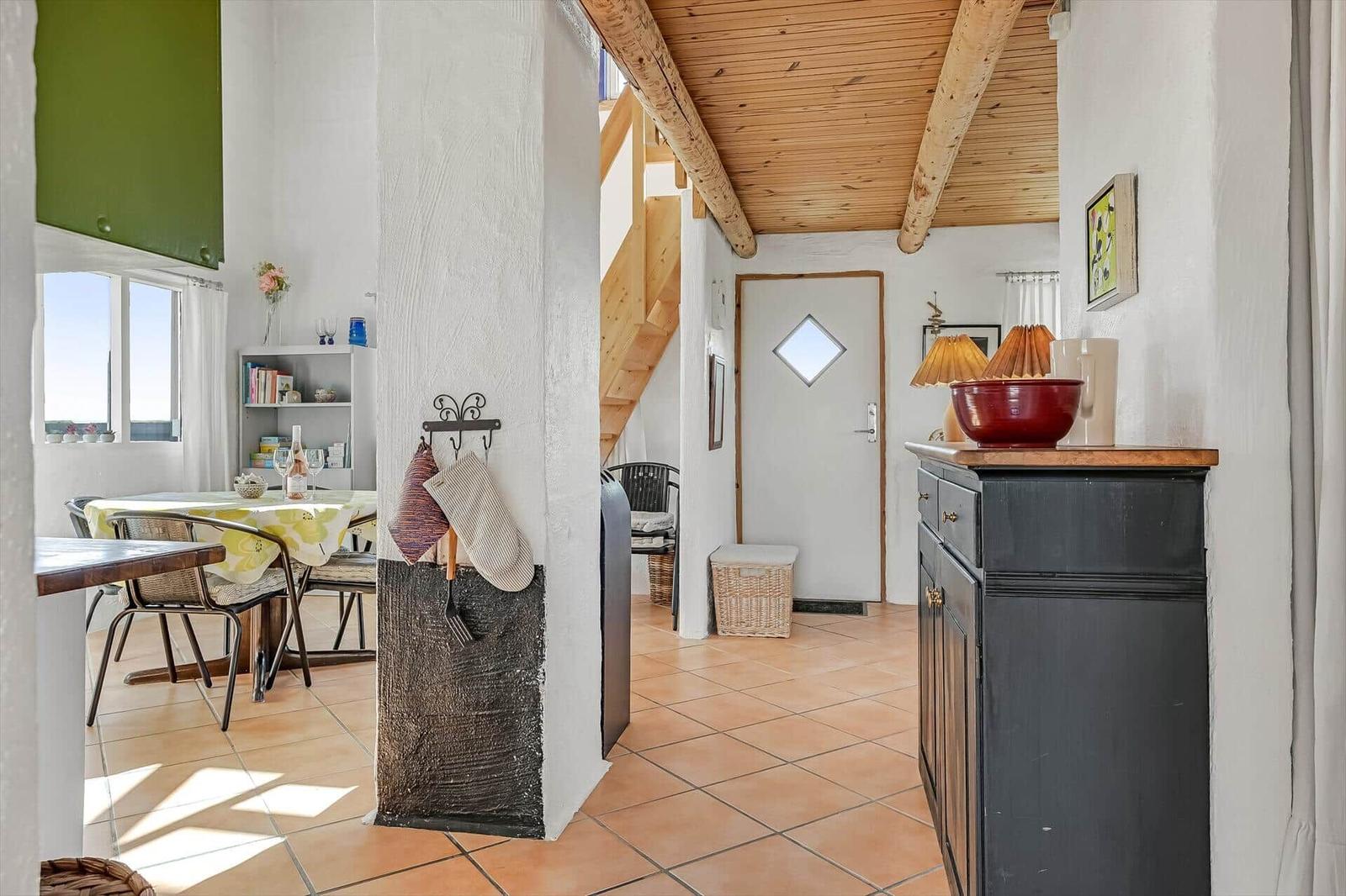 Flur mit Terrakottafliesen, schwarzem Sideboard und Holzbalkendecke zur Treppe.