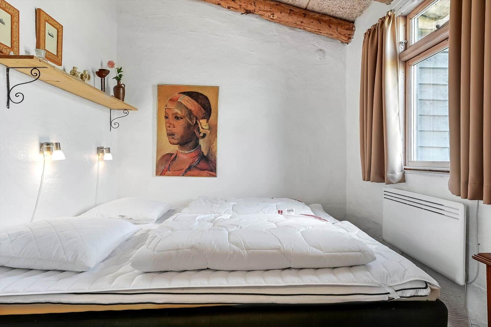 Doppelbett mit weißer Bettwäsche, Wandlampen und Fenster mit braunen Vorhängen.