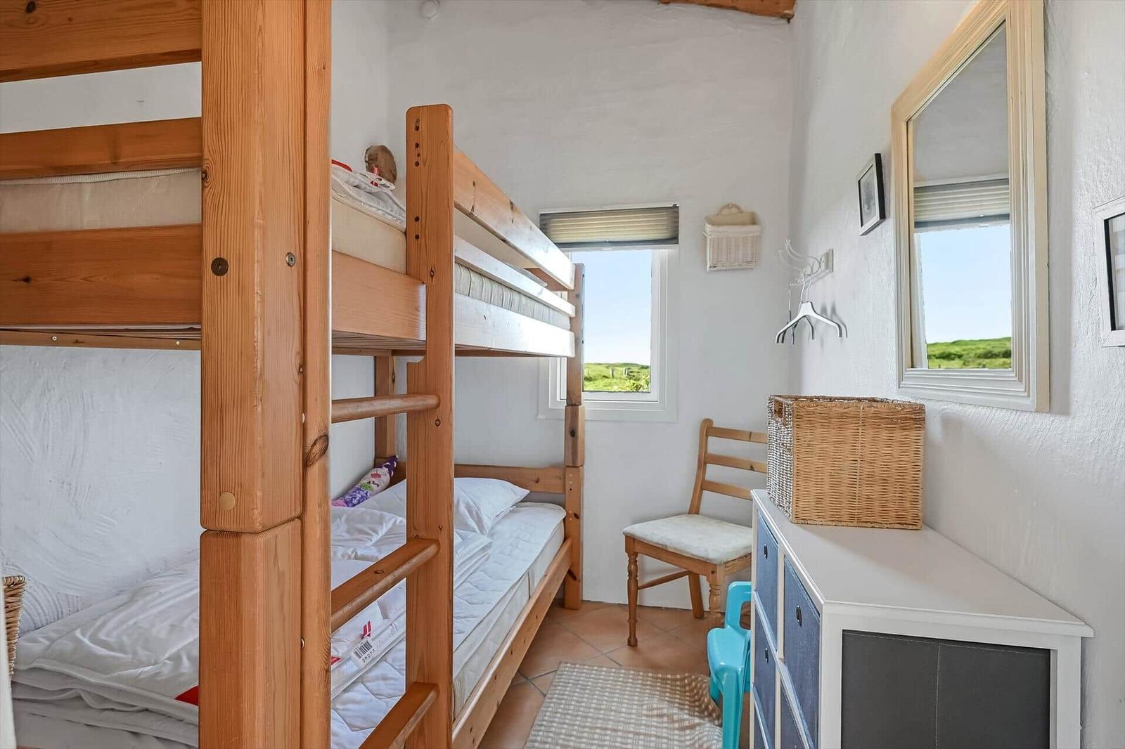 Schlafzimmer mit Holz-Etagenbett, weißer Kommode und Fensterblick ins Grüne.