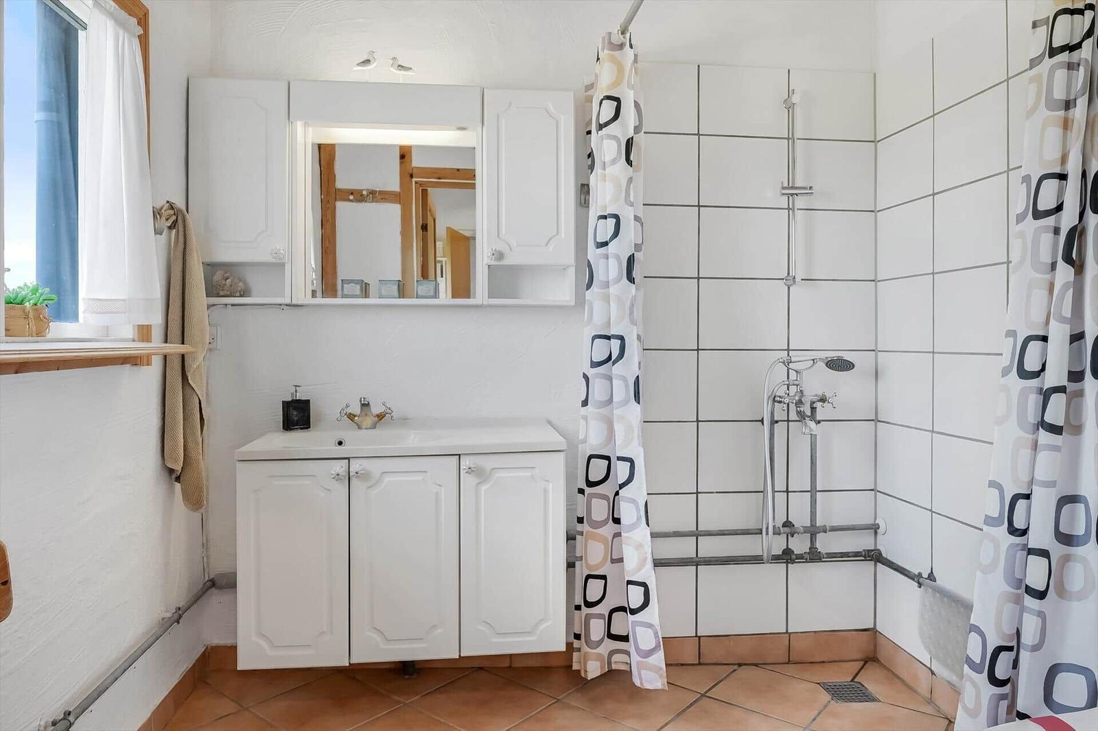 Badezimmer mit weißem Waschtisch, Spiegelschrank und gefliester Dusche mit Vorhang.