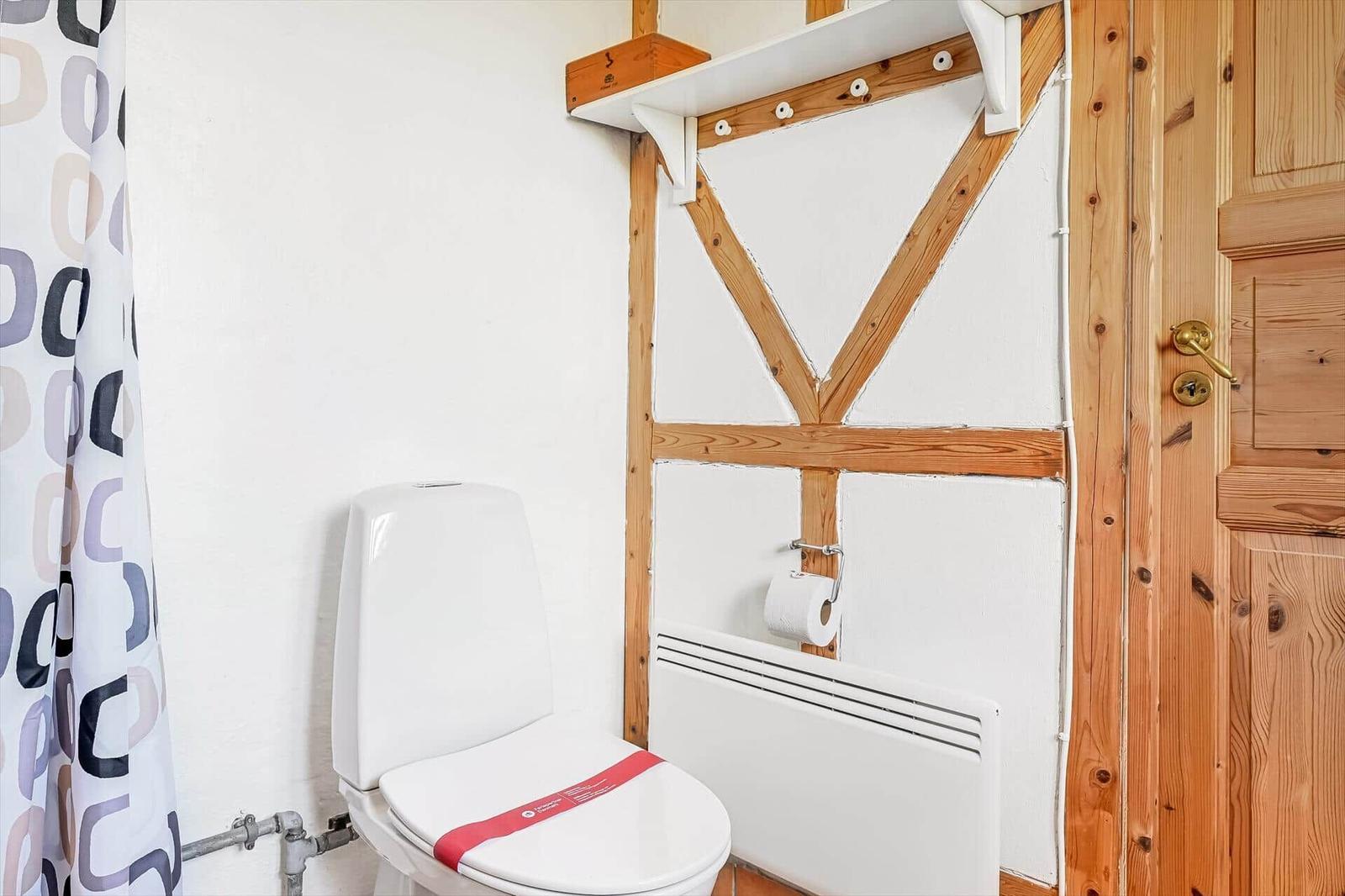 Badezimmer mit weißem WC, Fachwerkwand, Heizkörper und gemustertem Duschvorhang.