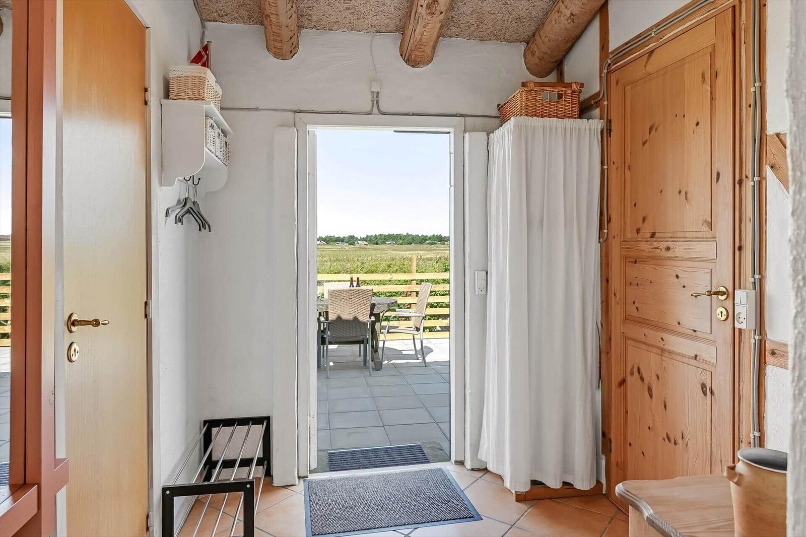 Eingang mit Holzbalkendecke, Terrakottafliesen und offener Tür zur Terrasse.