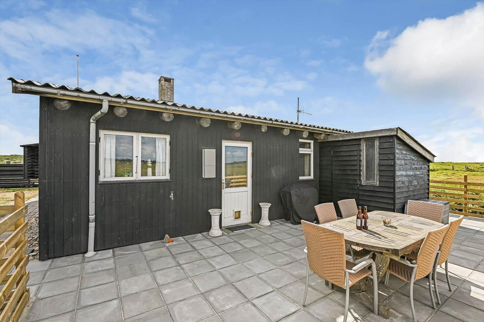 Terrasse mit Holztisch, Korbstühlen, Grill und schwarzer Holzwand.