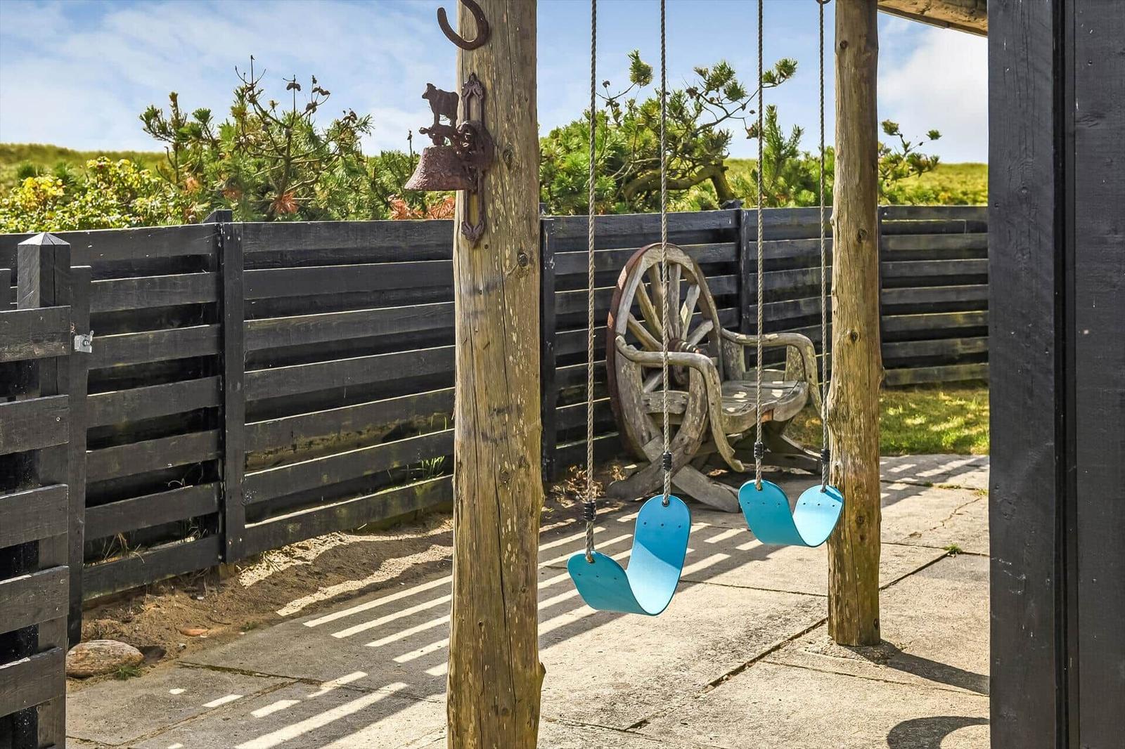 Überdachte Terrasse mit zwei blauen Schaukeln und Stuhl aus einem Wagenrad.