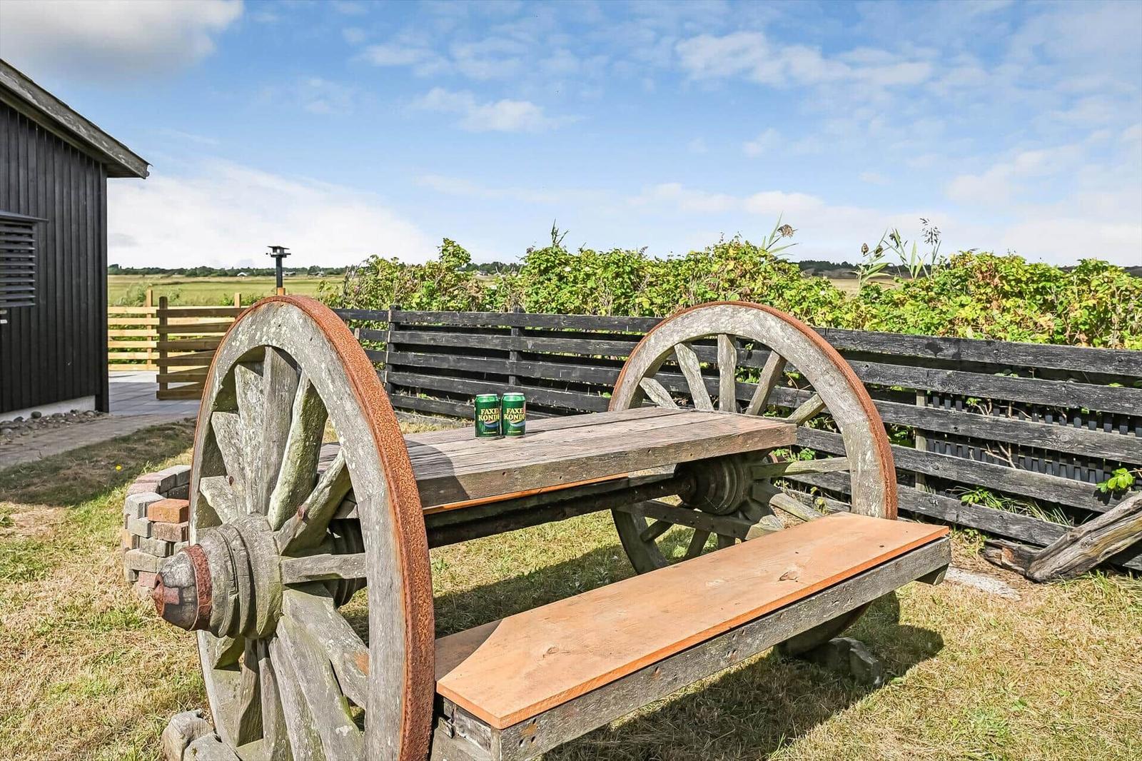 Gartenmöbel aus Wagenrädern mit Holztisch und Bank neben dunklem Zaun.