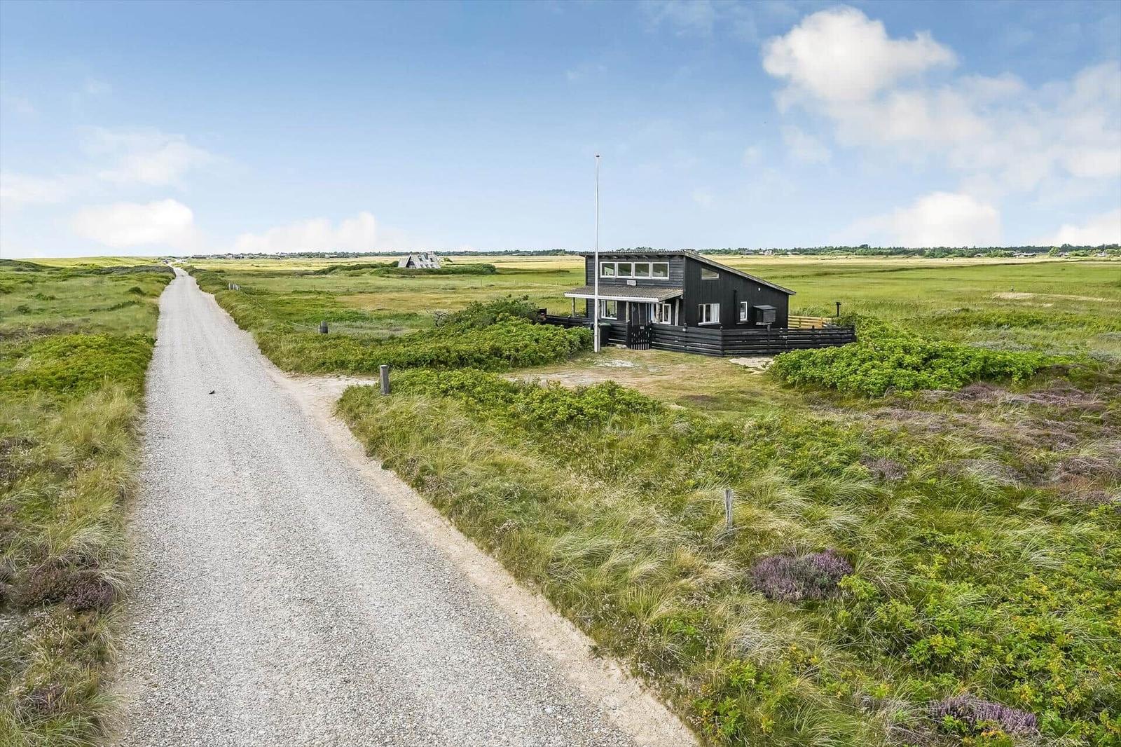 Schwarzes Holzhaus an Schotterweg in weiter Graslandschaft unter blauem Himmel.