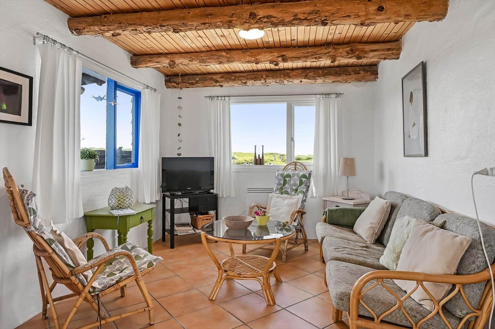 Wohnzimmer mit Sofa, Rattansesseln, Glastisch, Holzbalken und Fernseher.
