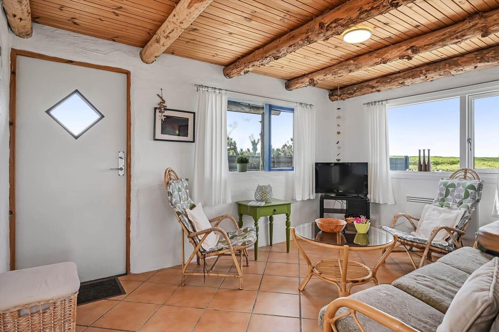 Wohnzimmer mit Rattansesseln, Glastisch, Fernseher und Tür mit Rautenfenster.