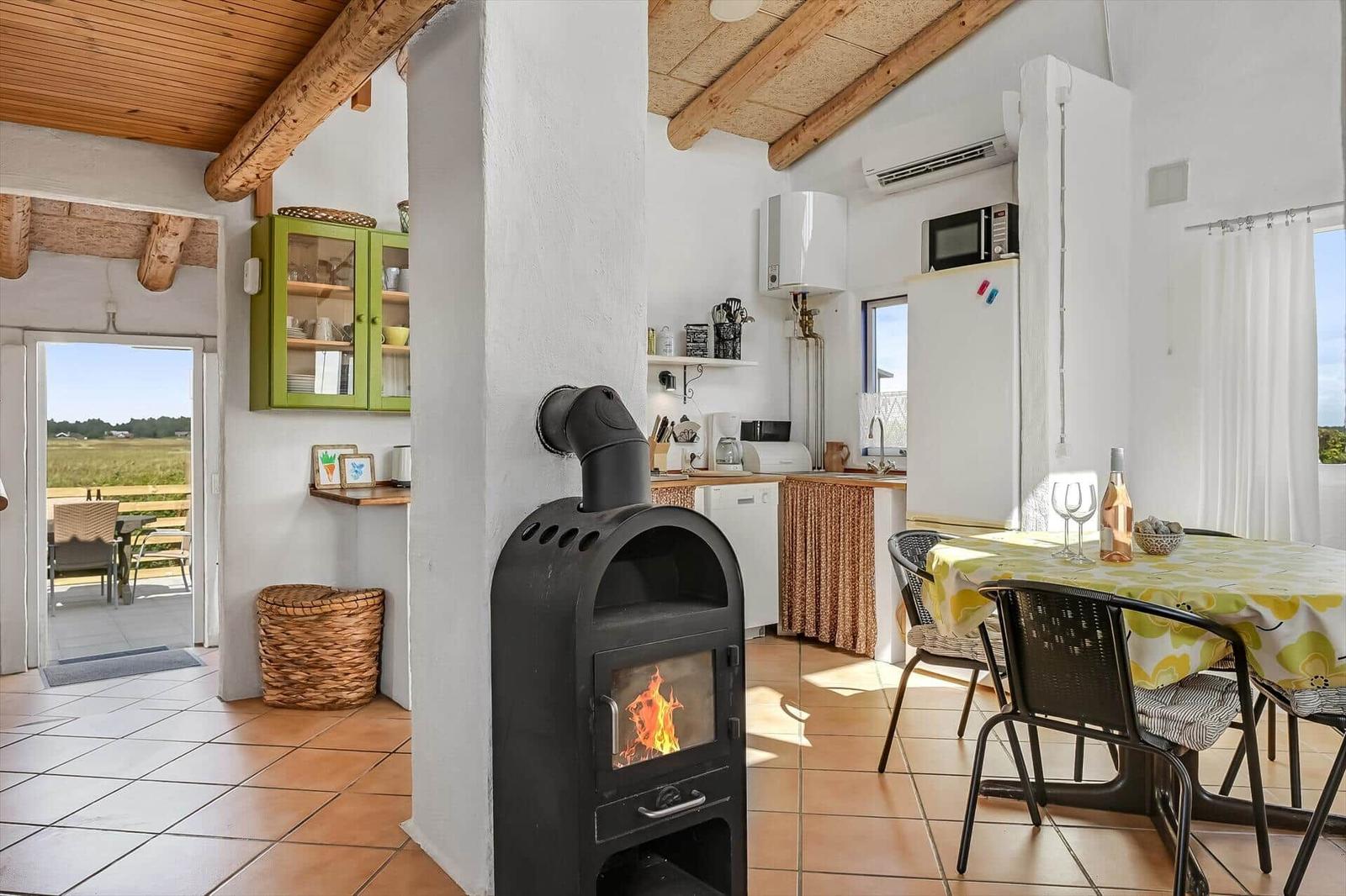 Wohnküche mit Kaminofen, Esstisch, Küchenzeile und Holzbalken an der Decke.