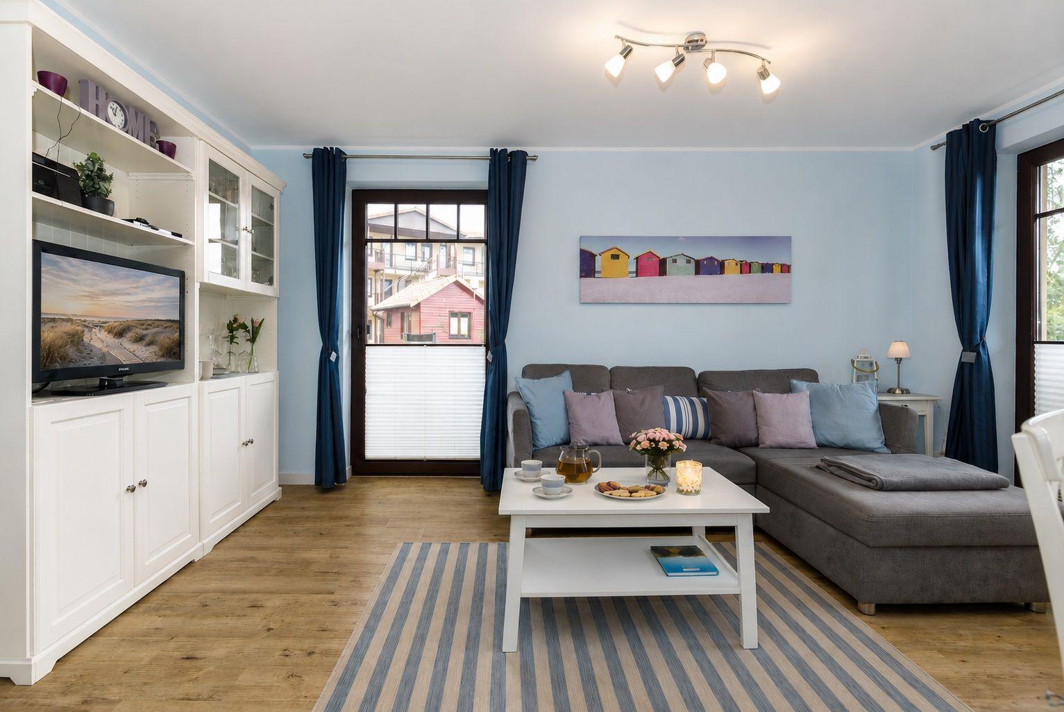 Wohnzimmer mit grauem Sofa, weißem Couchtisch und blauen Vorhängen.