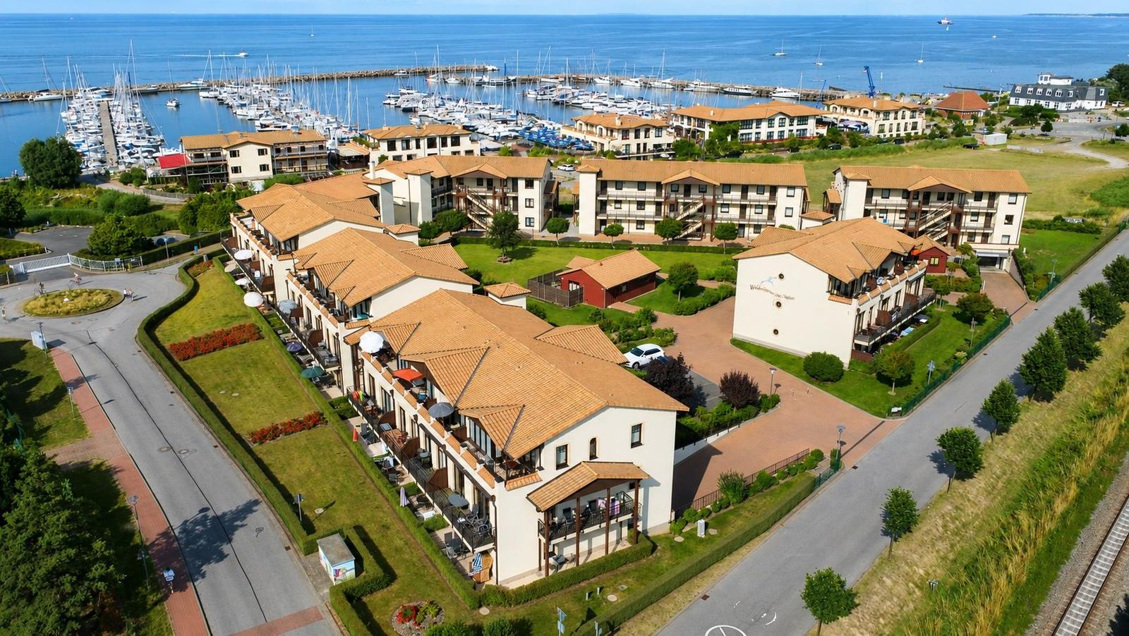 Wohnanlage mit Terrassen und Blick auf Hafen mit Segelyachten.