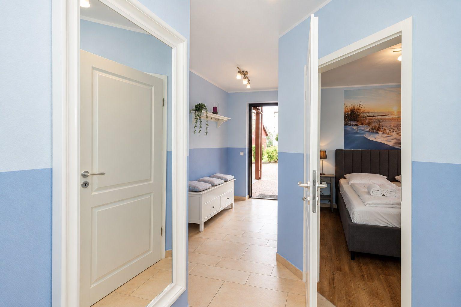 Flur mit Schlafzimmer und Tür zur Terrasse. Wandfarbe blau-weiß. Bett mit Kissen und Decke.