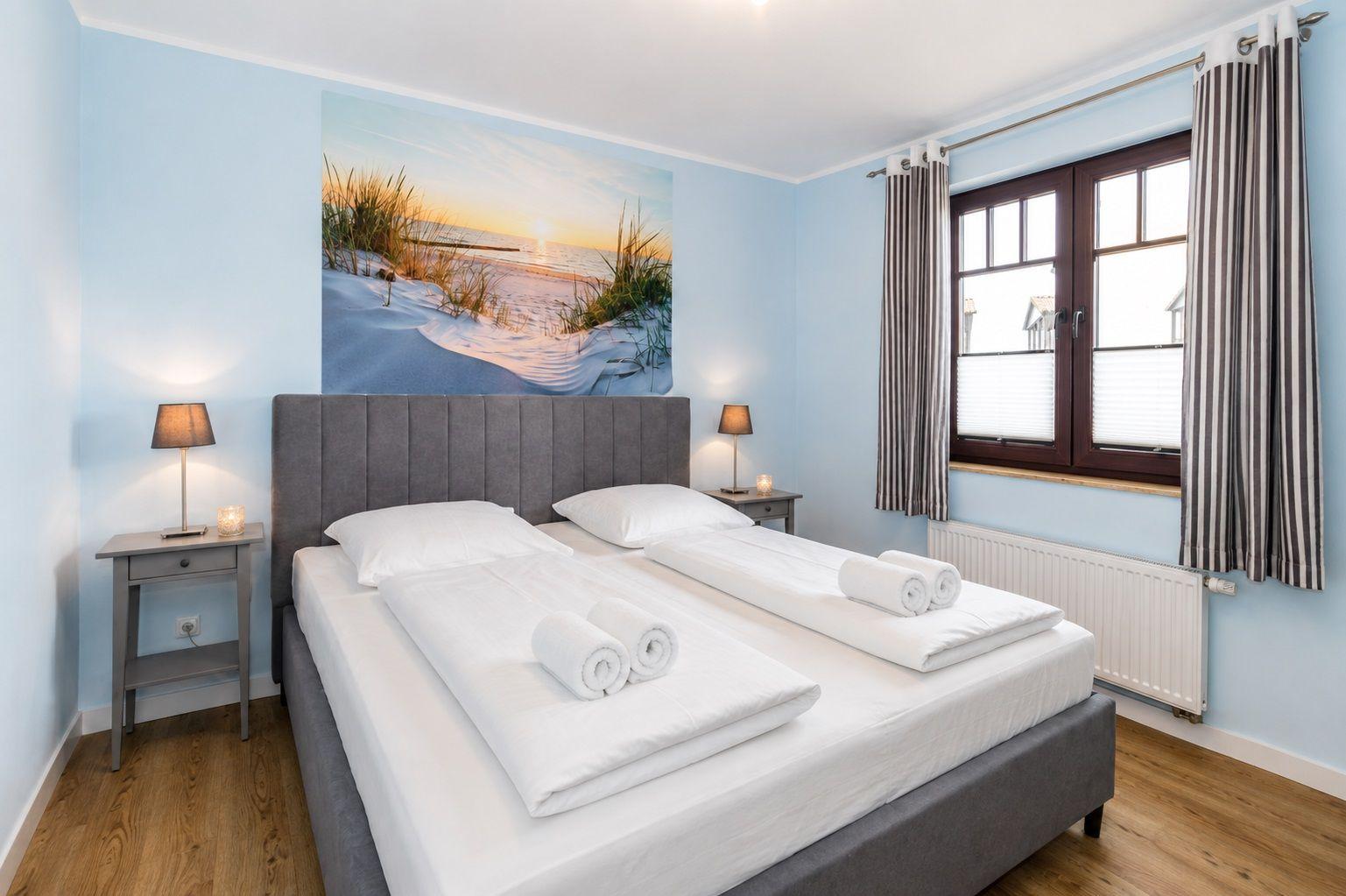Schlafzimmer mit Bett, Nachttischen und Wandbild. Fenster mit Vorhängen.