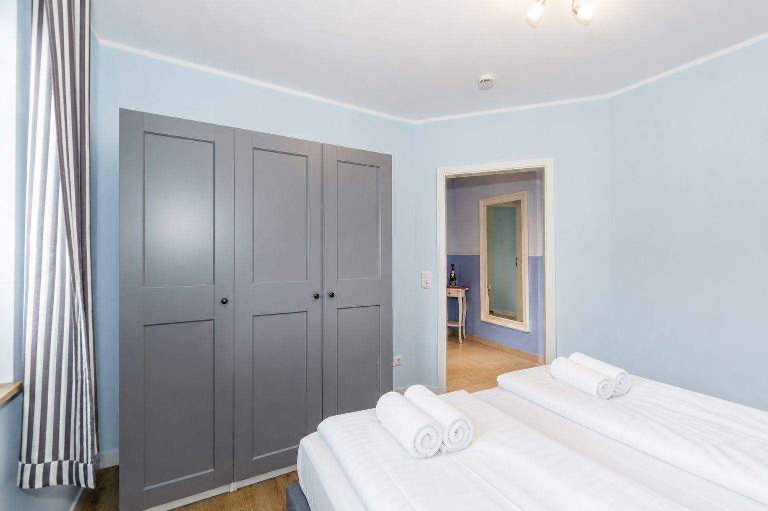 Schlafzimmer mit Bett, Kleiderschrank und Blick in angrenzenden Raum.