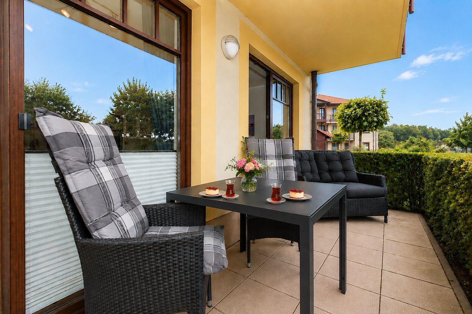 Terrasse mit Tisch, Stühlen und Sitzgruppe. Blick auf grüne Hecke und Ferienhaus.