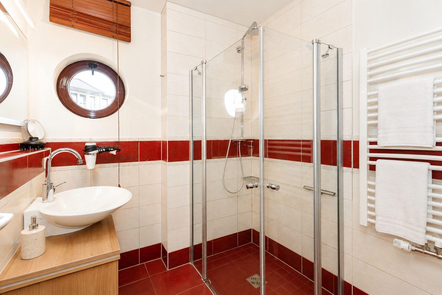Badezimmer mit Dusche, Waschbecken und runden Fenster.