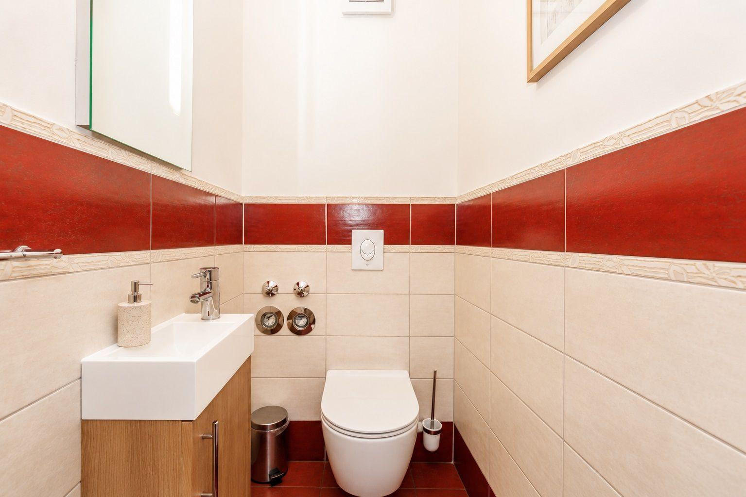 Badezimmer mit Toilette, Waschbecken und Spiegel. Wandfliesen in Rot- und Beigetönen.