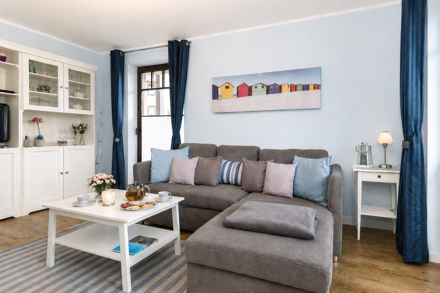 Wohnzimmer mit grauem Sofa, weißem Tisch und blauen Vorhängen an der Wand.