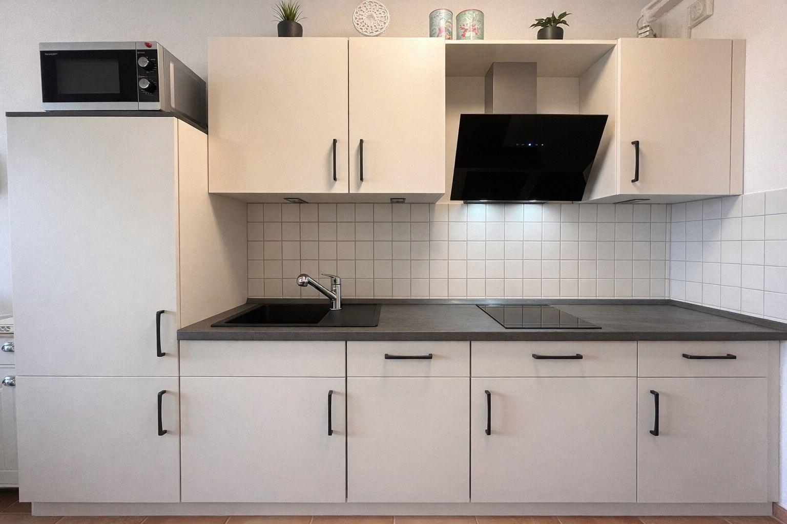 Küche mit weißen Schränken, dunkler Arbeitsplatte, Spüle und Herd.