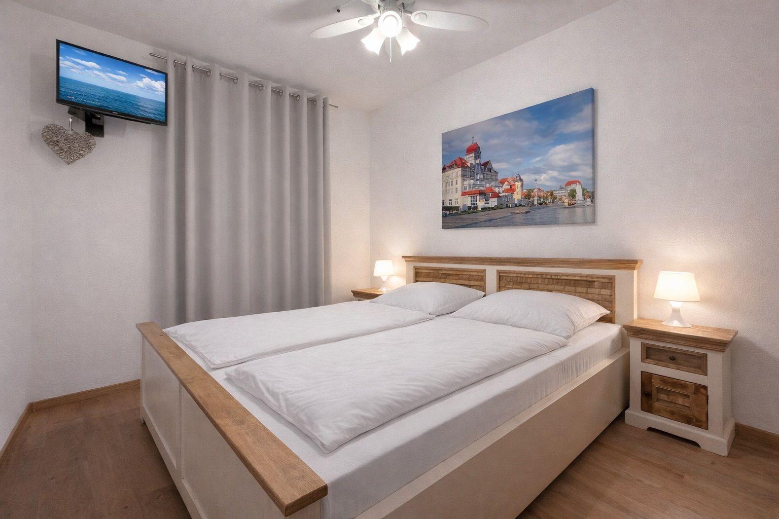 Schlafzimmer mit Doppelbett, Nachttischen und Wandbild. Fernseher an der Wand.