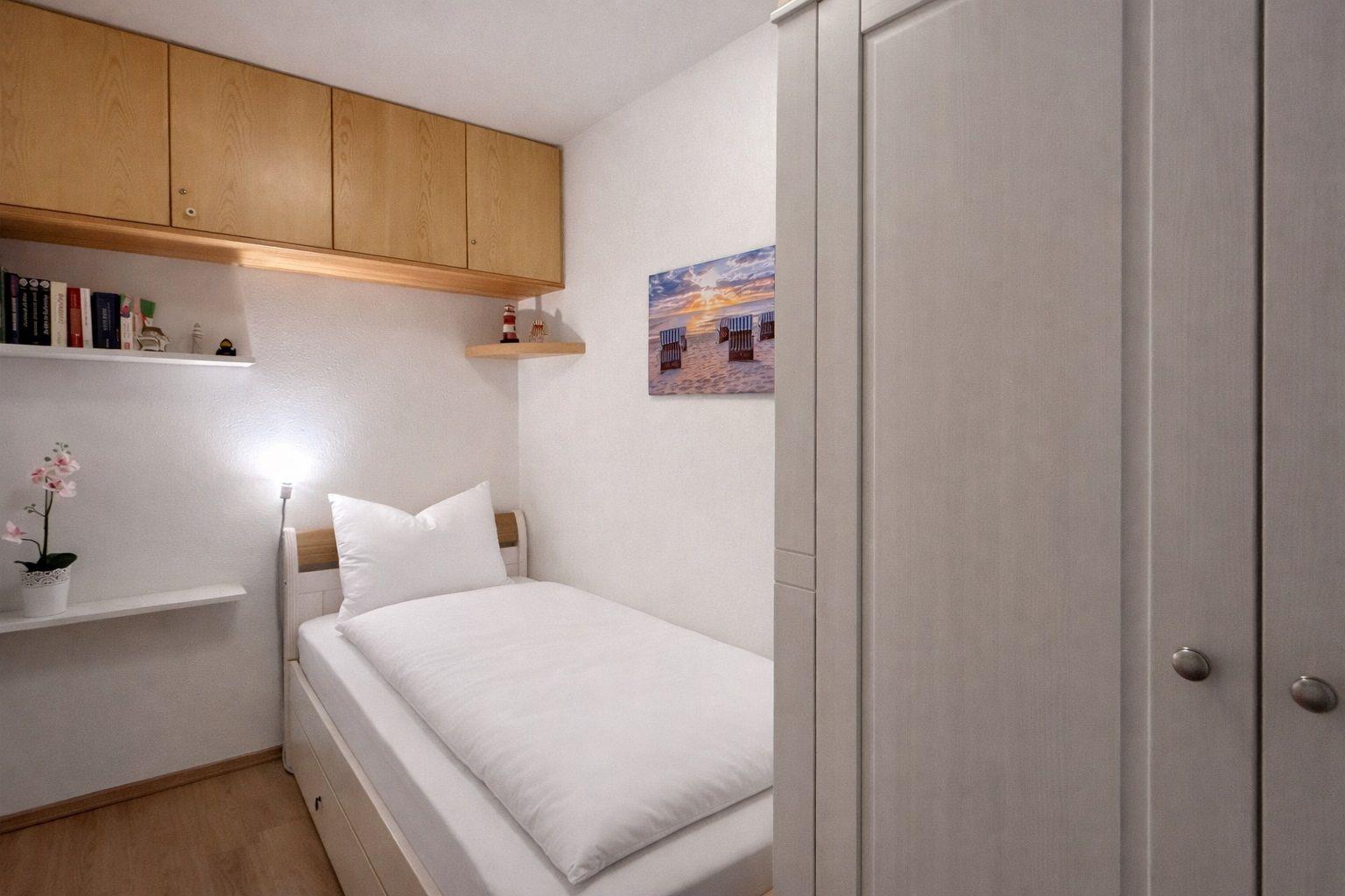 Ein Schlafzimmer mit Einzelbett, Schrank und Wandregalen mit Dekoration.