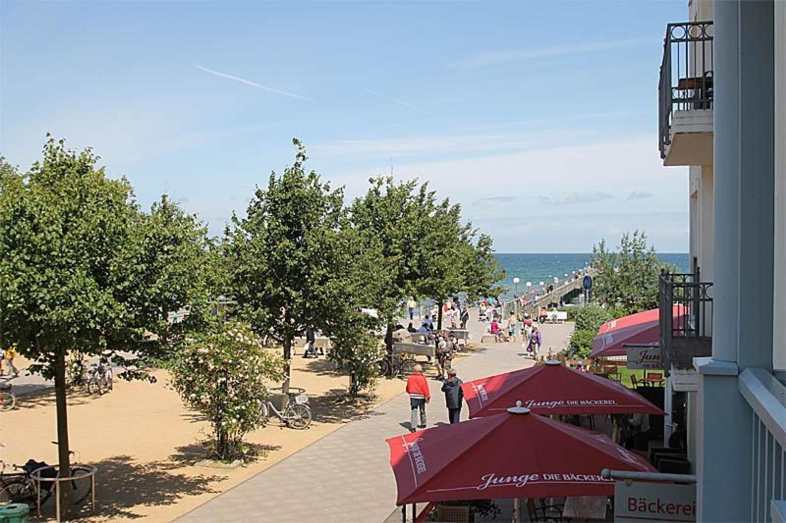 Blick auf Strandpromenade mit Bäumen, Menschen und roten Markisen.