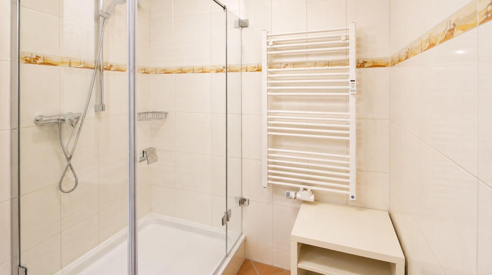 Dusche mit Glaswand, Heizkörper und kleinem Tisch.