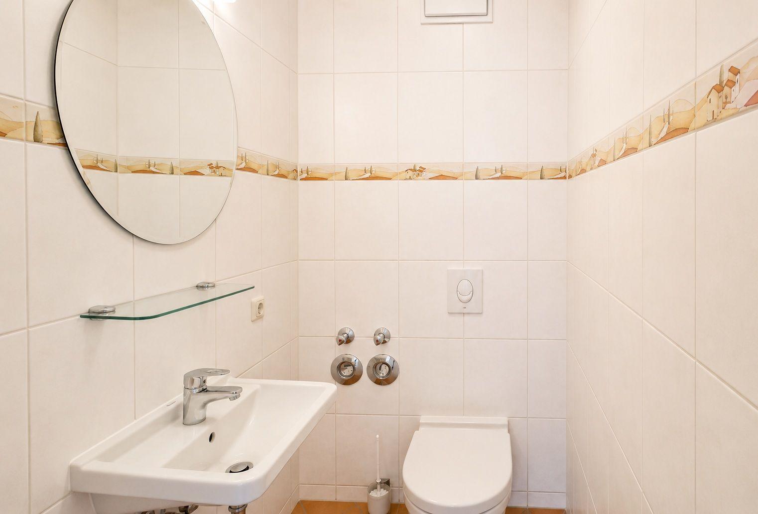 Badezimmer mit Waschbecken, Spiegel und Toilette. Wandfliesen mit dekorativer Bordüre.