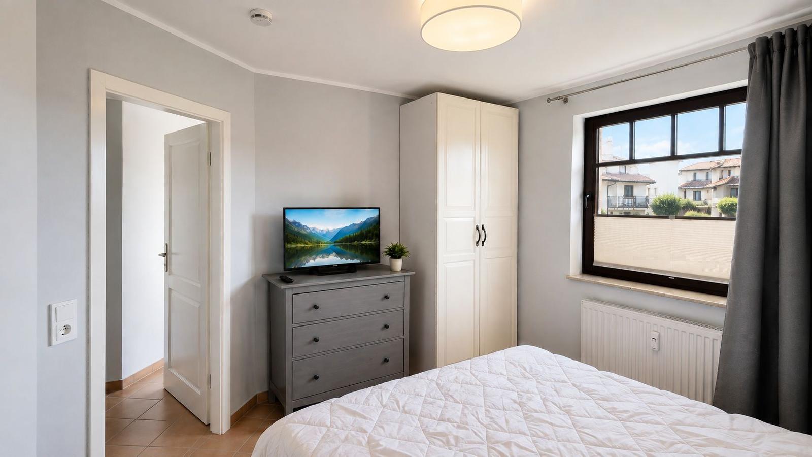 Schlafzimmer mit Bett, Kleiderschrank, TV und Fenster mit Jalousie.