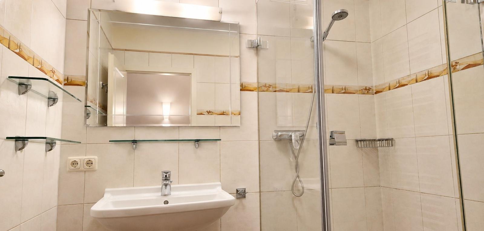 Badezimmer mit Dusche, Waschbecken und Spiegel. Fliesen mit dekorativer Bordüre.