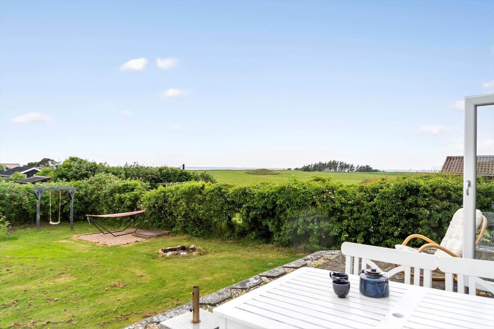 Terrasse mit weißem Holzbank und geschlossenem Sonnenschirm neben Whirlpool und Pflanzen.